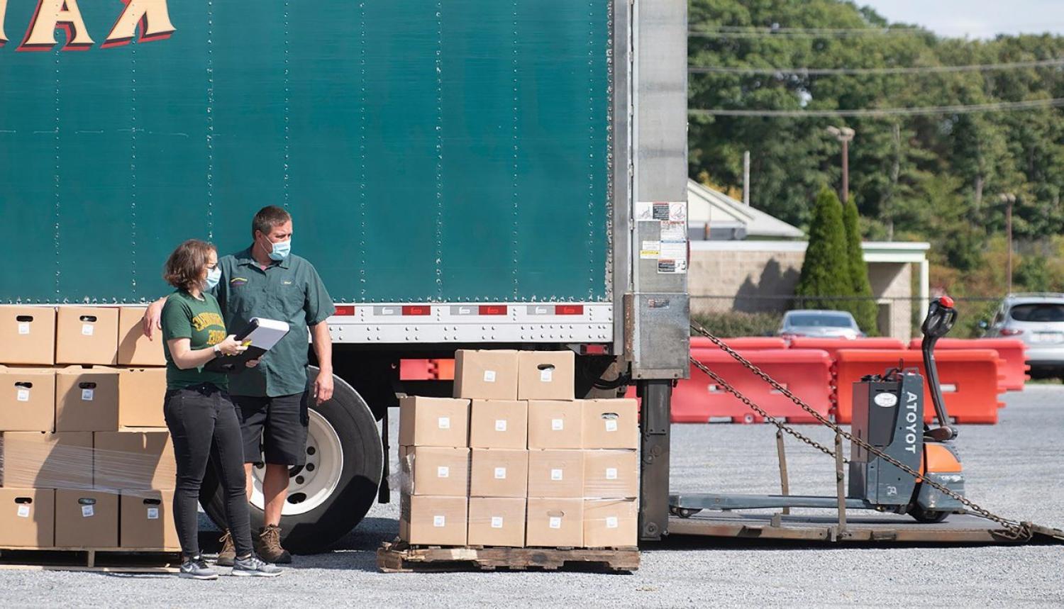 Two people standing next to a truck and piles of boxes